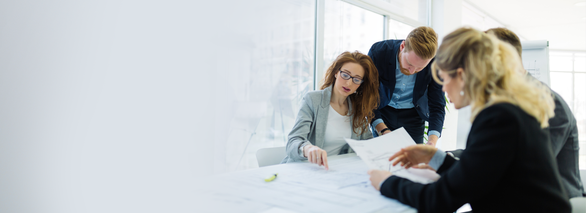 Four professionals collaborating at a table with documents in a bright office.